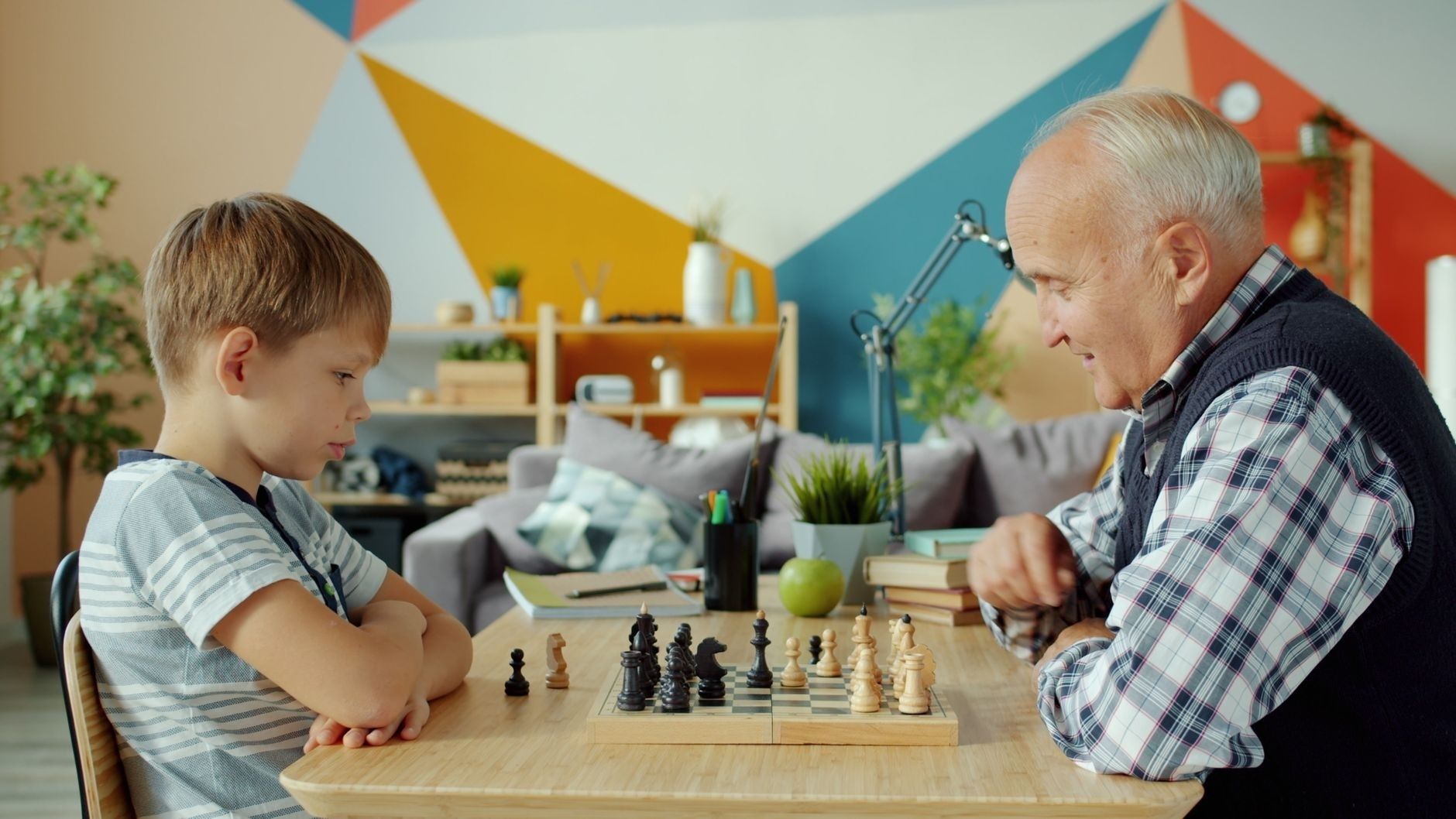 Ett barn och en äldre man spelar schack vid ett bord