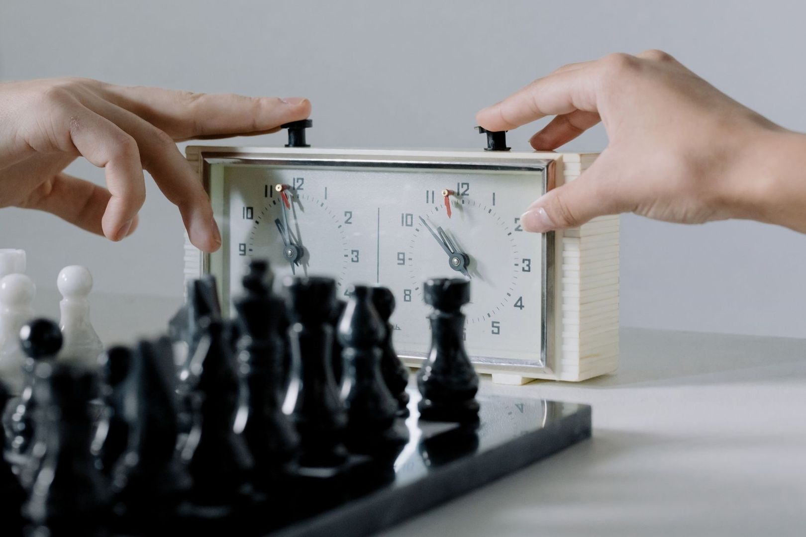 Analog schackklocka med två urtavlor bakom svarta schackpjäser